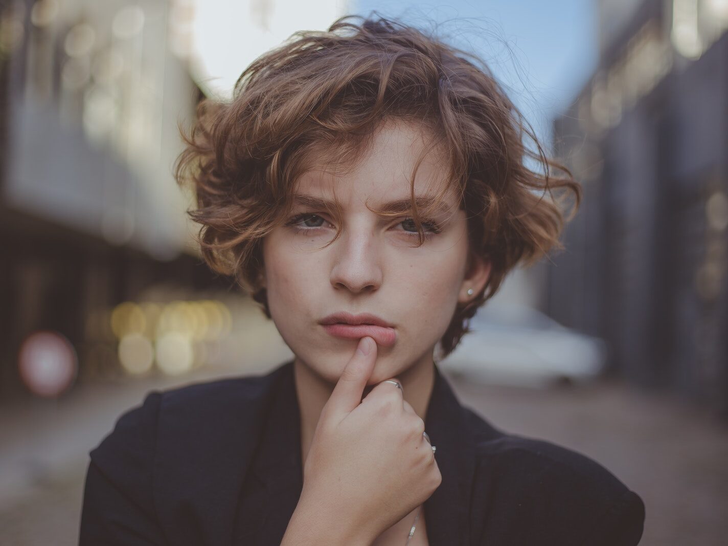 Selective Focus Portrait Photo of Woman Posing with Her Thumb Below Her Lip