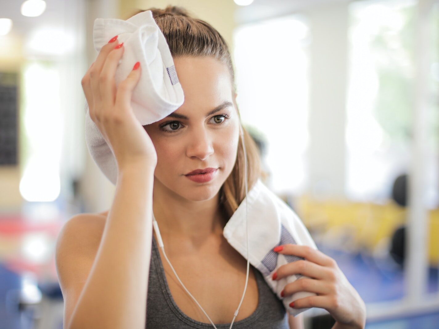 Selective Focus Close-up Photo of Woman in Gray Tank Top Using White Towel to Wipe Her Face