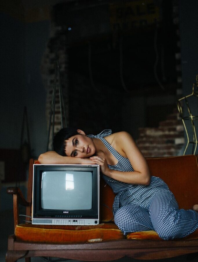 Peaceful female wearing overall lying on vintage TV set sitting on seethe in tailor workshop for sale