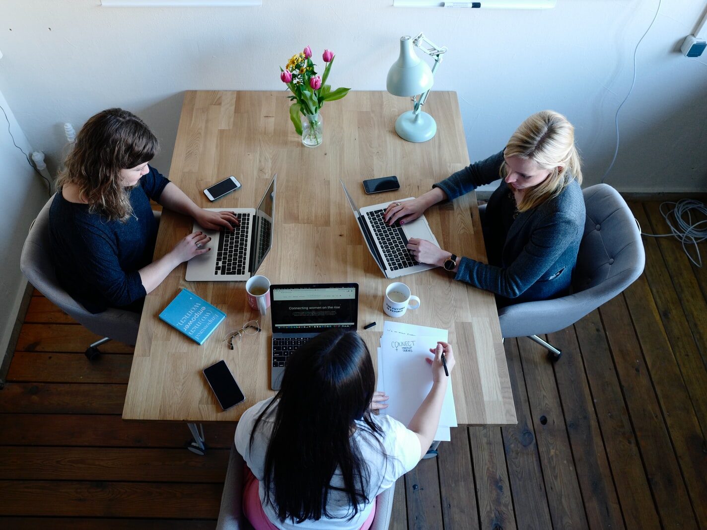 three women sitting around table using laptops