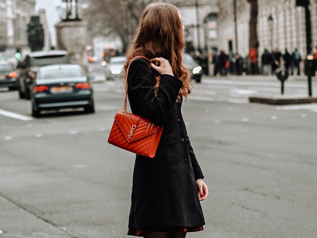 woman in black coat standing on sidewalk during daytime
