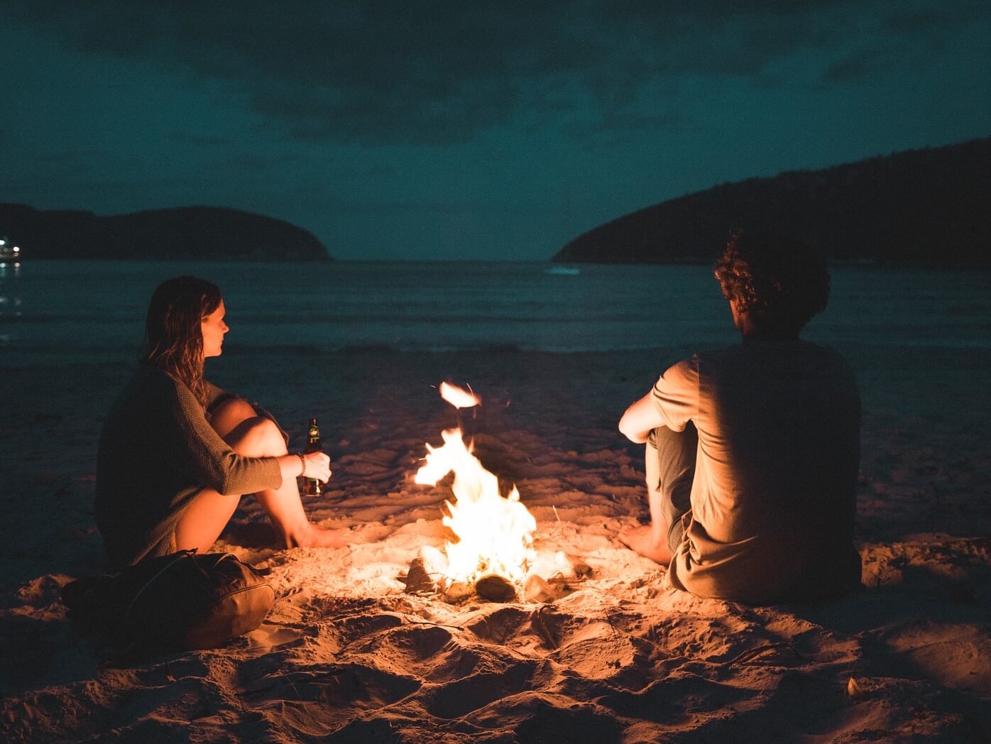 man and woman with bone fire sitting on seashore
