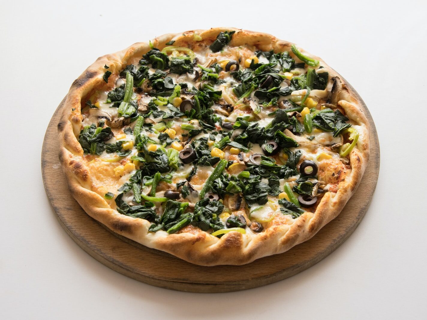 pizza with green leaves and cheese on brown wooden round plate