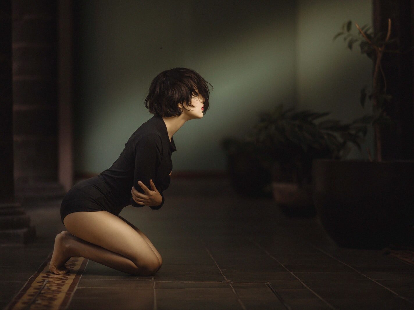 woman kneeling with arms folded over chest inside dim-lit room