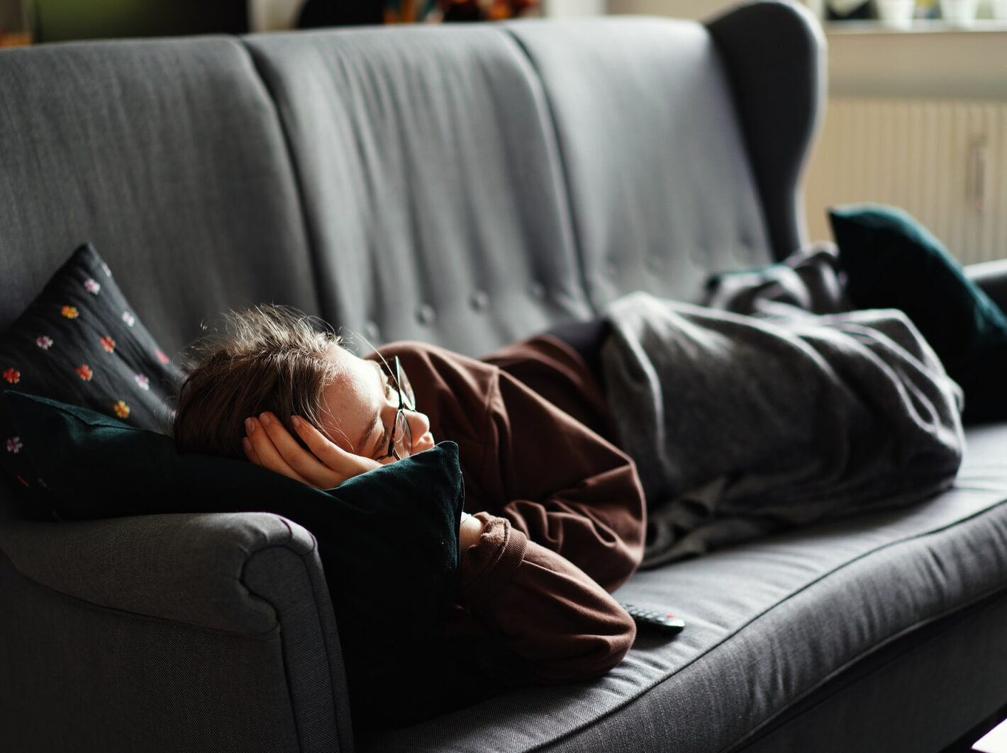 woman in pink jacket lying on gray couch