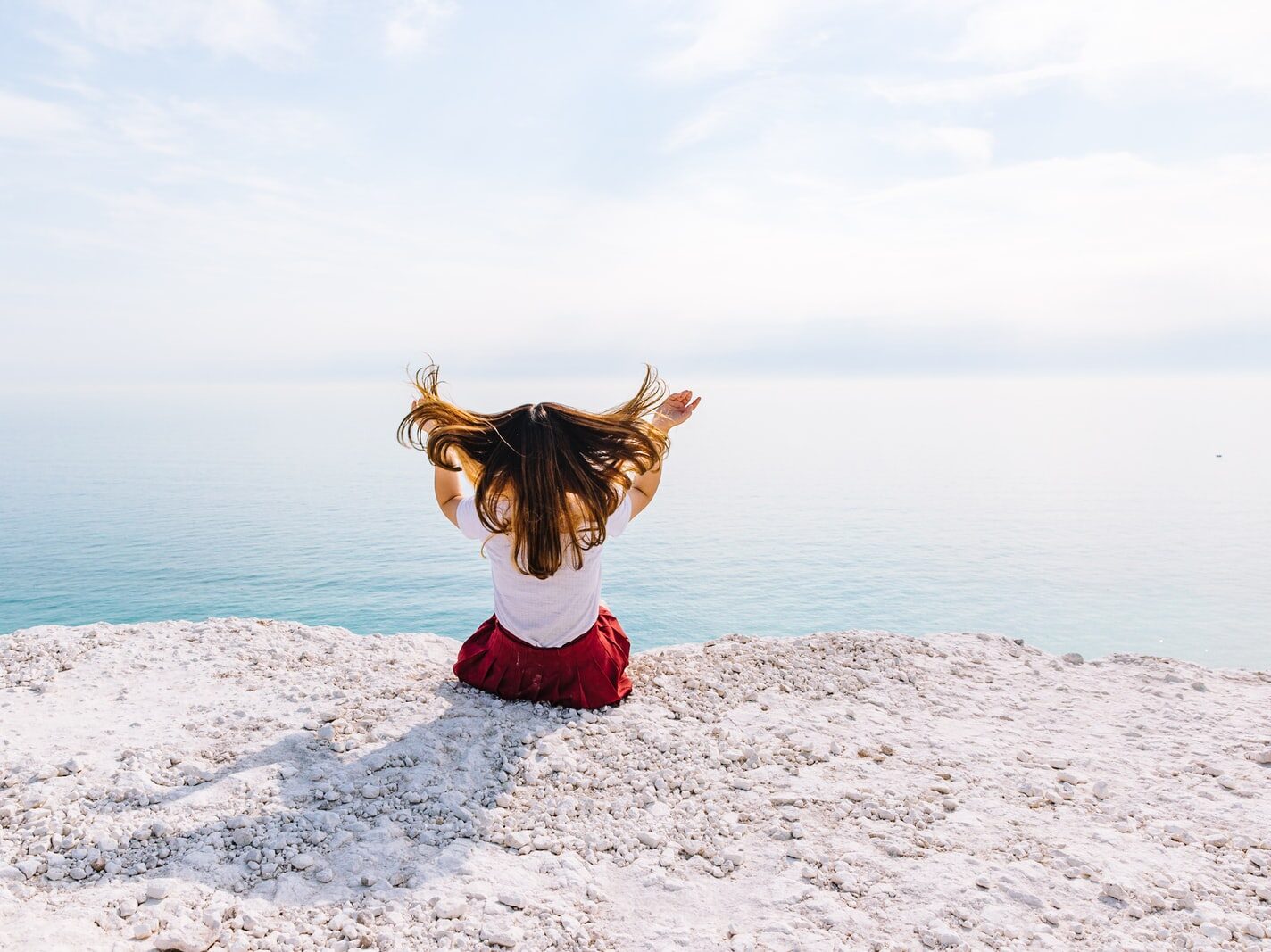 woman sitting on cliff near body of water