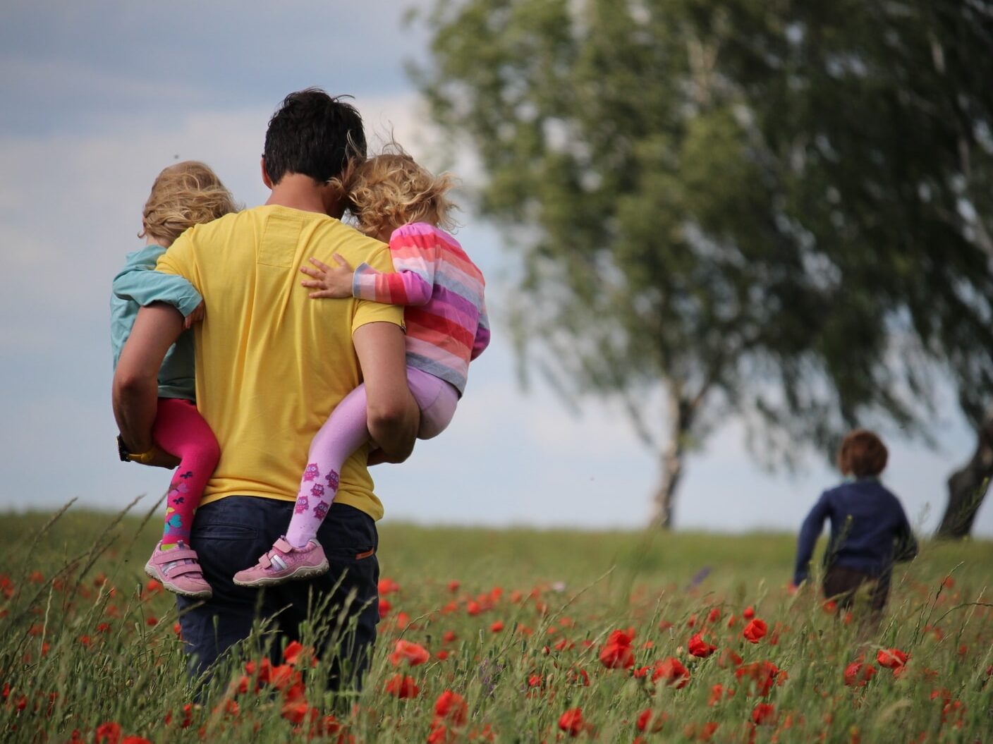 man carrying to girls on field of red petaled flower