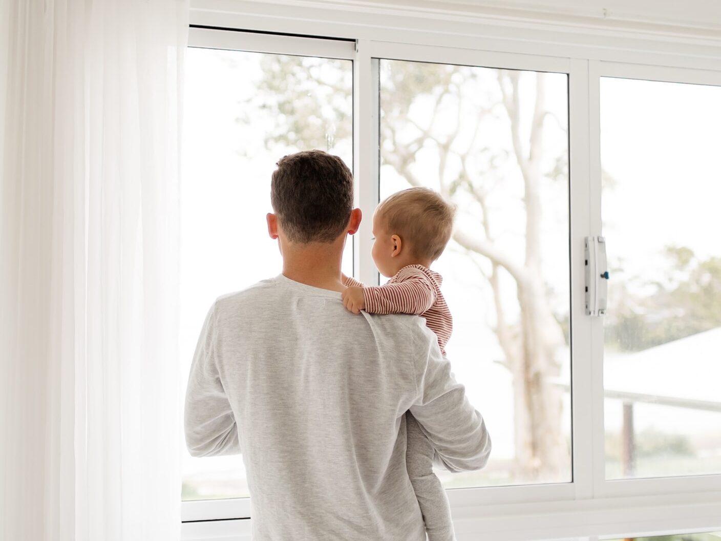 boy in gray sweater standing beside window during daytime