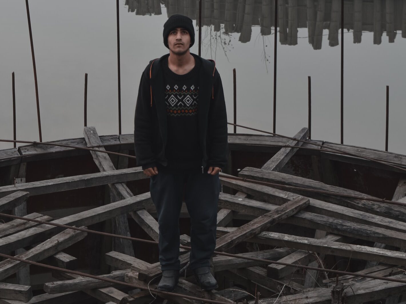 man in black and red hoodie standing on wooden dock during daytime