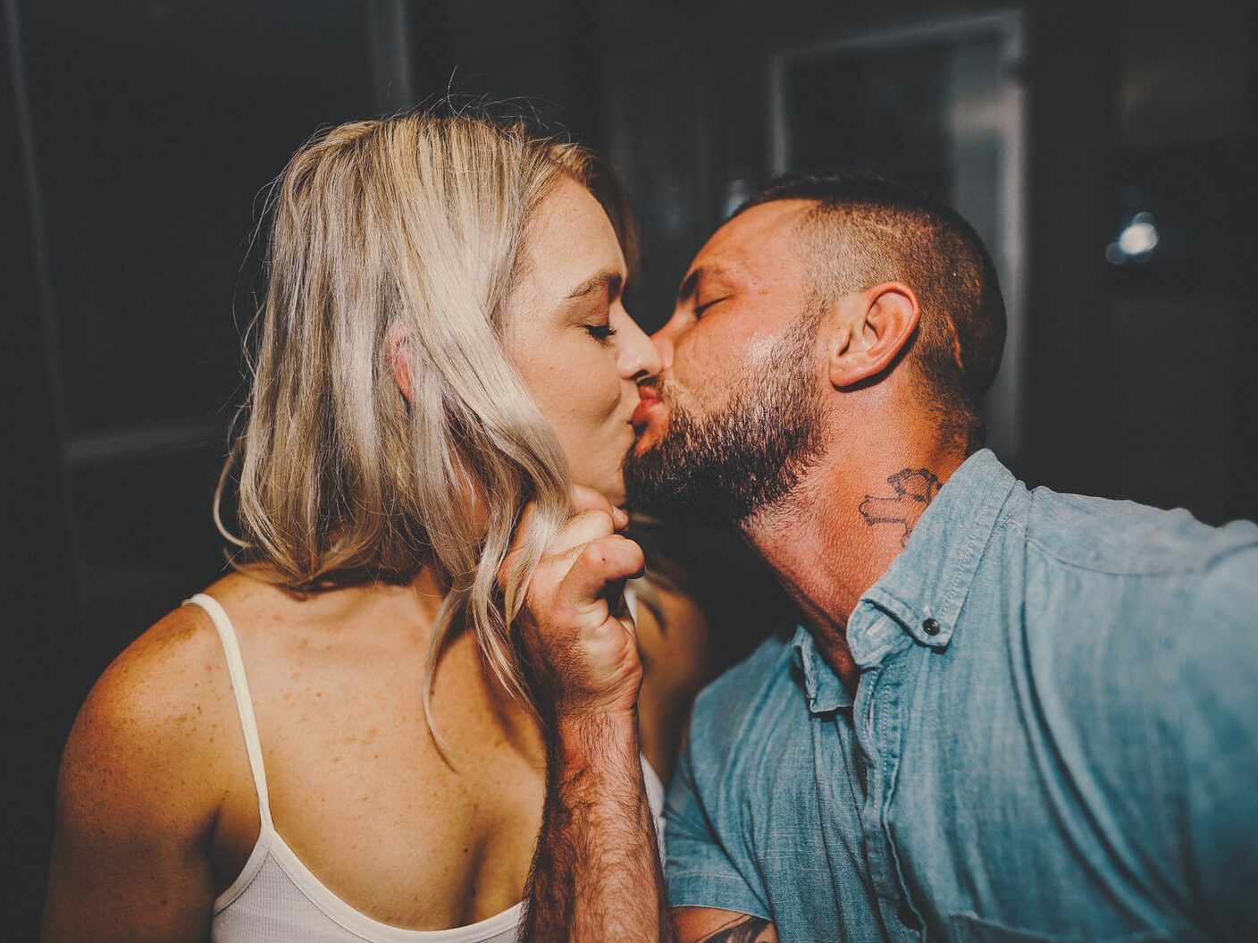 man in blue button up shirt kissing woman in white spaghetti strap top