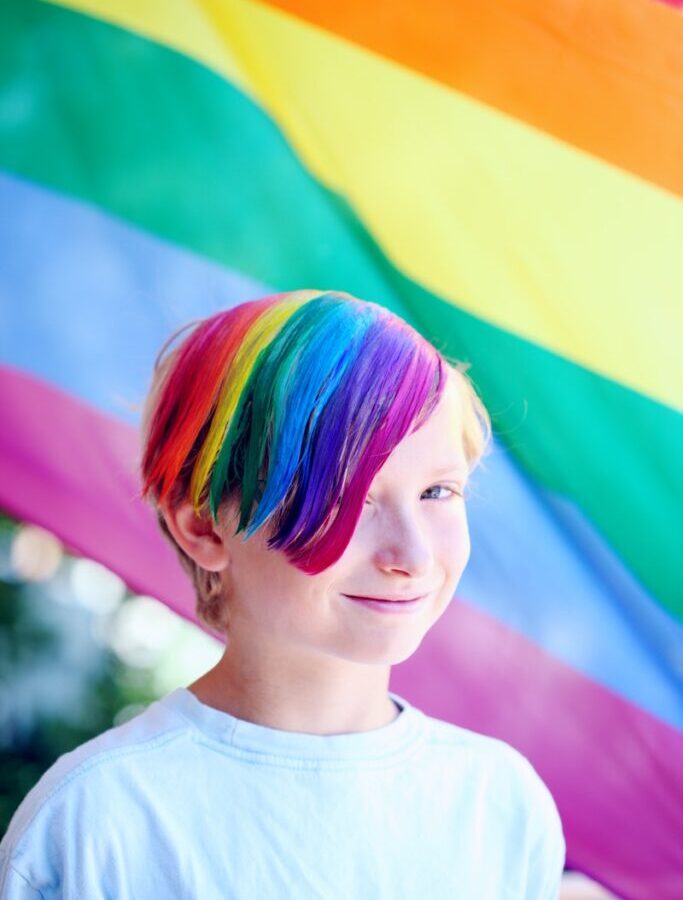 Boy Wearing White Shirt With Iridescent Hair Color Infront of Flag