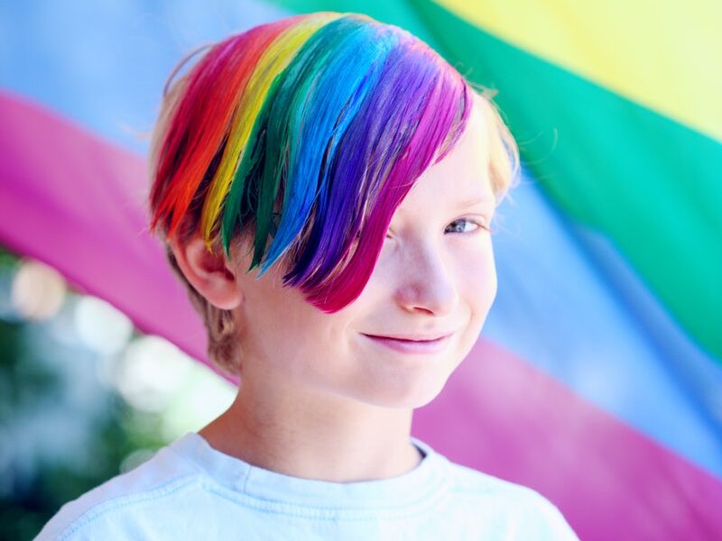 Boy Wearing White Shirt With Iridescent Hair Color Infront of Flag