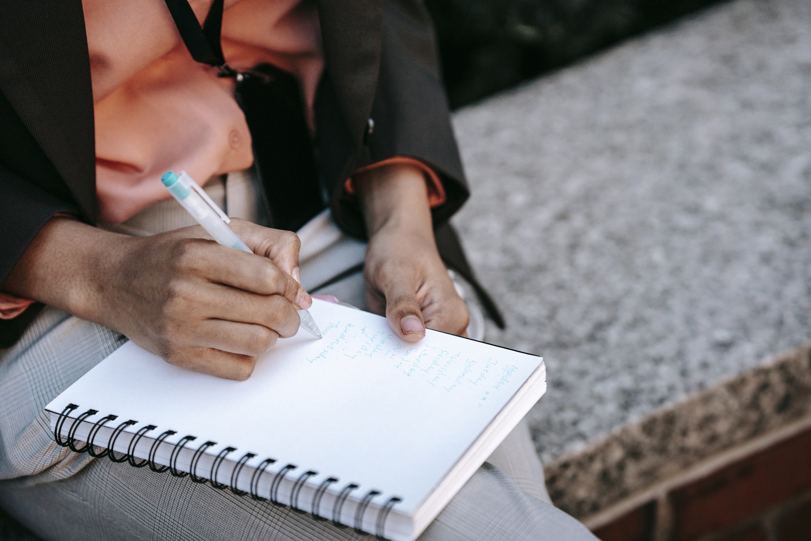 From above of crop anonymous ethnic woman making list in notebook during work in park