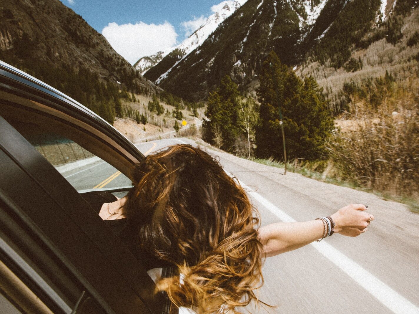 woman riding on vehicle putting her head and right arm outside the window while travelling the road