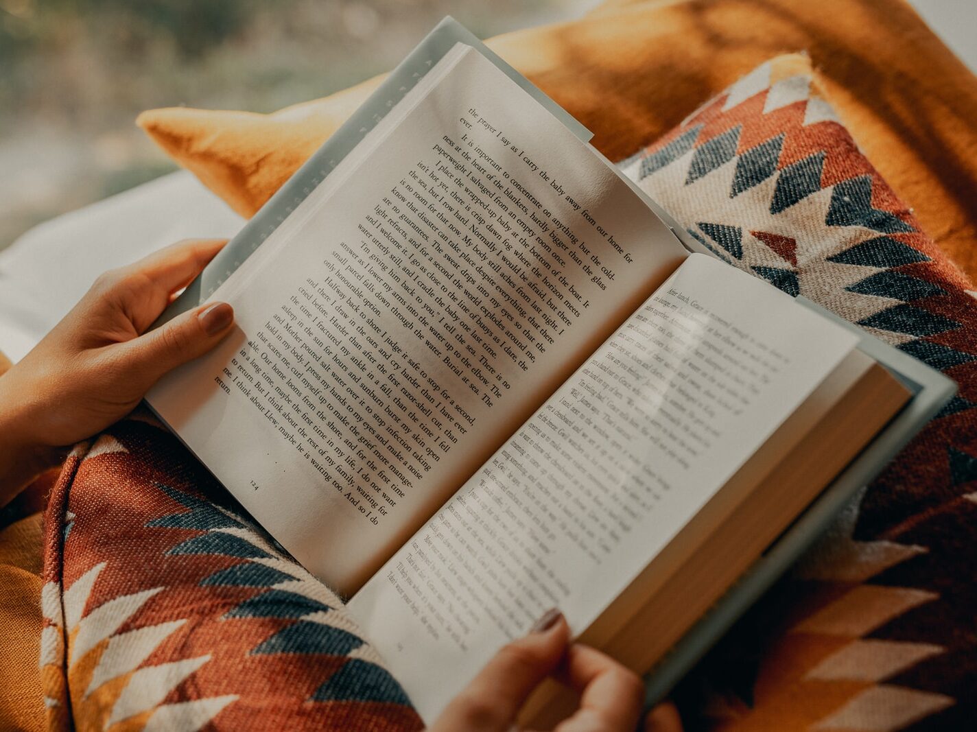person reading book on brown and beige textile