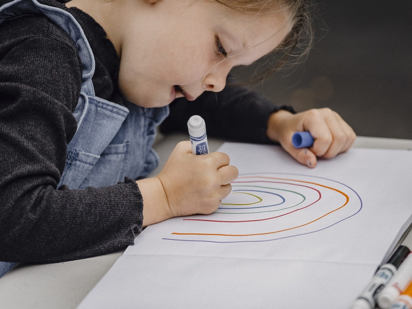 Little girl drawing rainbow on paper