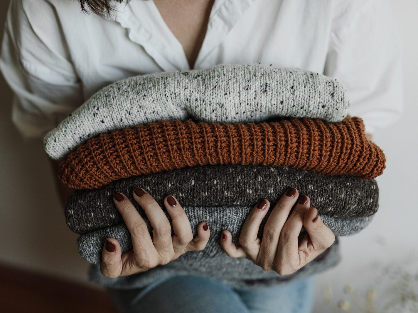 A Close-up Shot of a Person Holding a Stack of Folded Knitted Fabrics