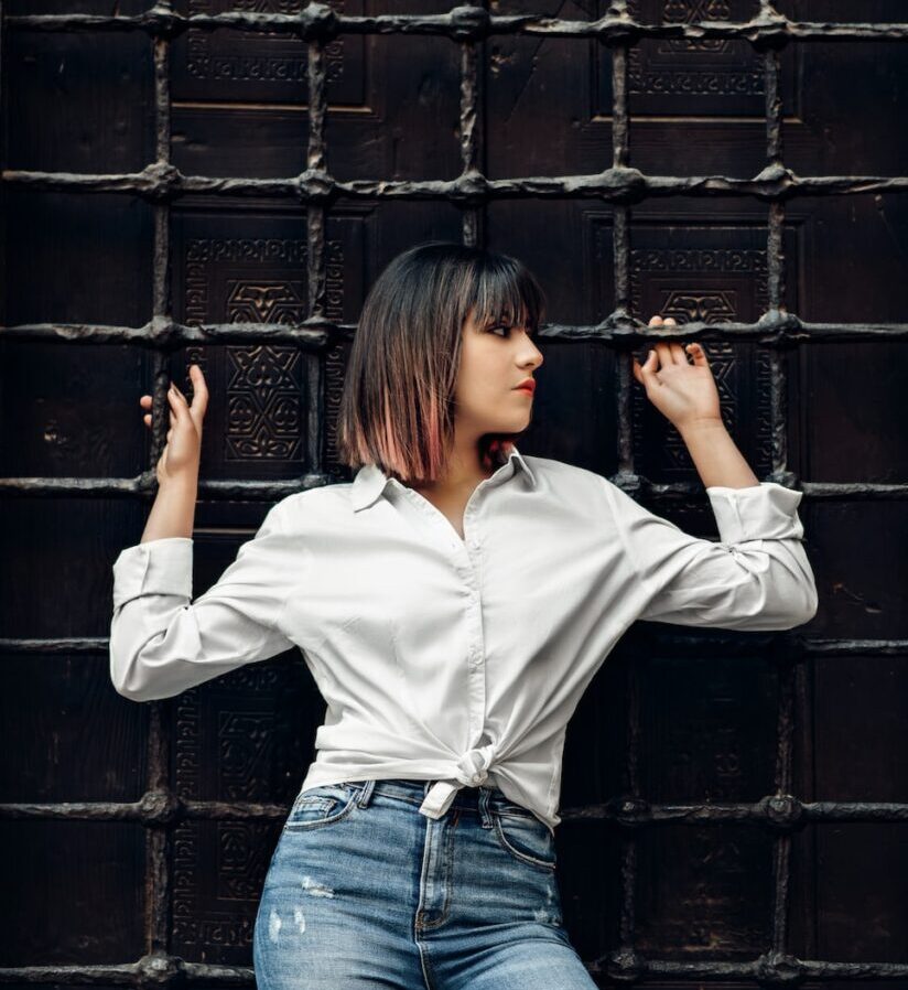 woman in white dress shirt leaning and holding on metal mesh wall