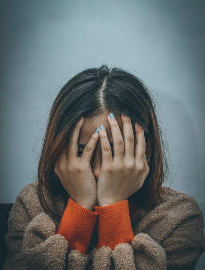 woman in brown sweater covering her face with her hand