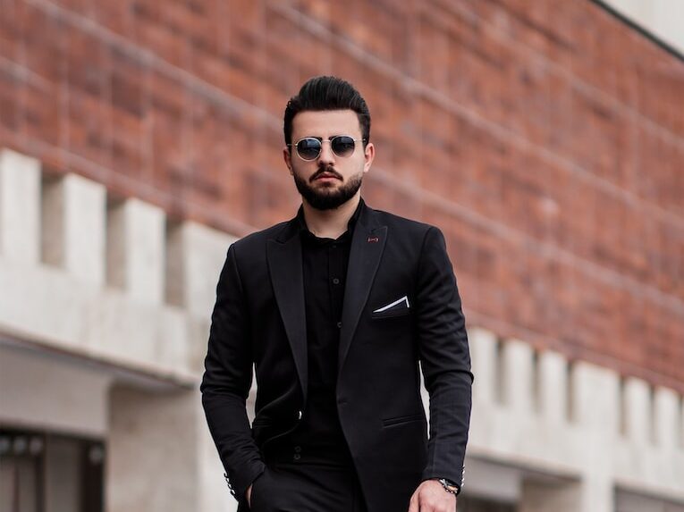 man in black suit jacket and black pants standing on gray concrete floor during daytime