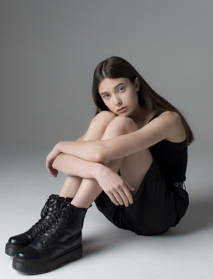 Teenage Girl with Long Black Hair Sitting on Floor and Looking Sadly at Camera