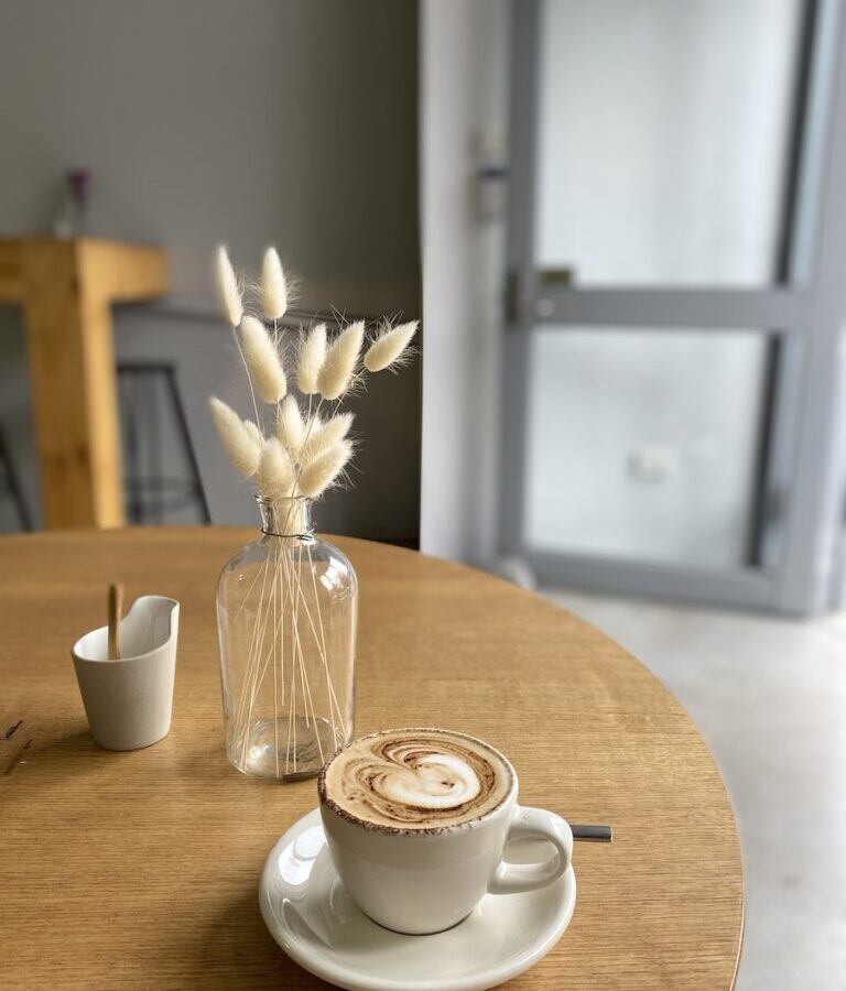 White Ceramic Cup on Saucer Beside Flower Vase on Table