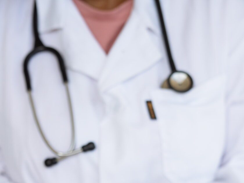 Faceless ethnic medical worker in lab coat and stethoscope taking of transparent gloves after approaching patients for examination in modern hospital