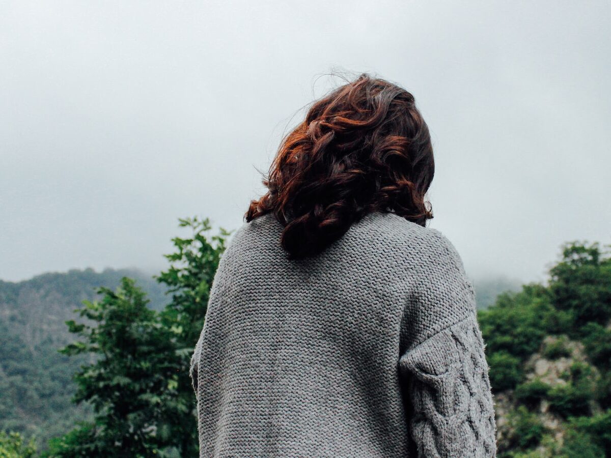 woman in gray sweater standing in front of trees during daytime