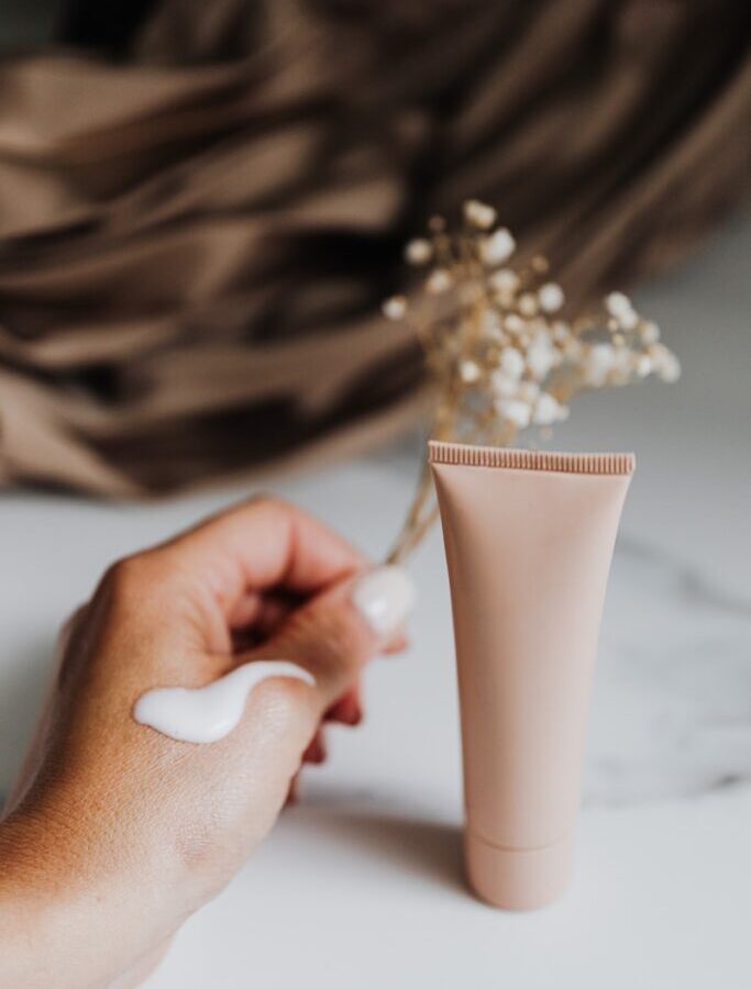 Person Holding Flowers Near Tube Hand Cream