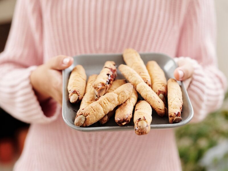 A Girl Wearing A Witch Hat With A Tray Of Witch Fingers Bread Design