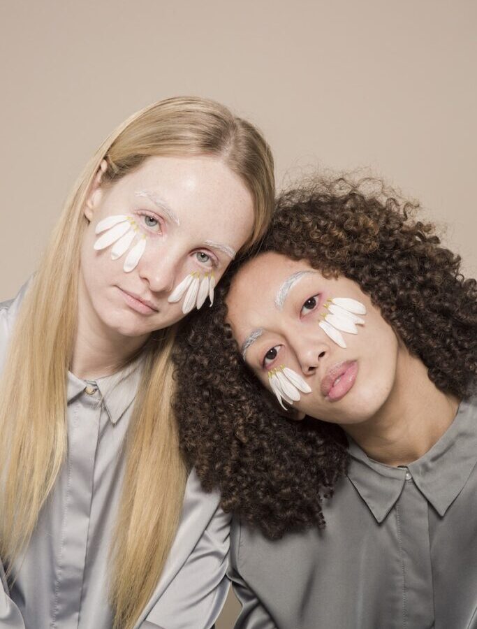 Confident multiethnic ladies with white petals on face in studio
