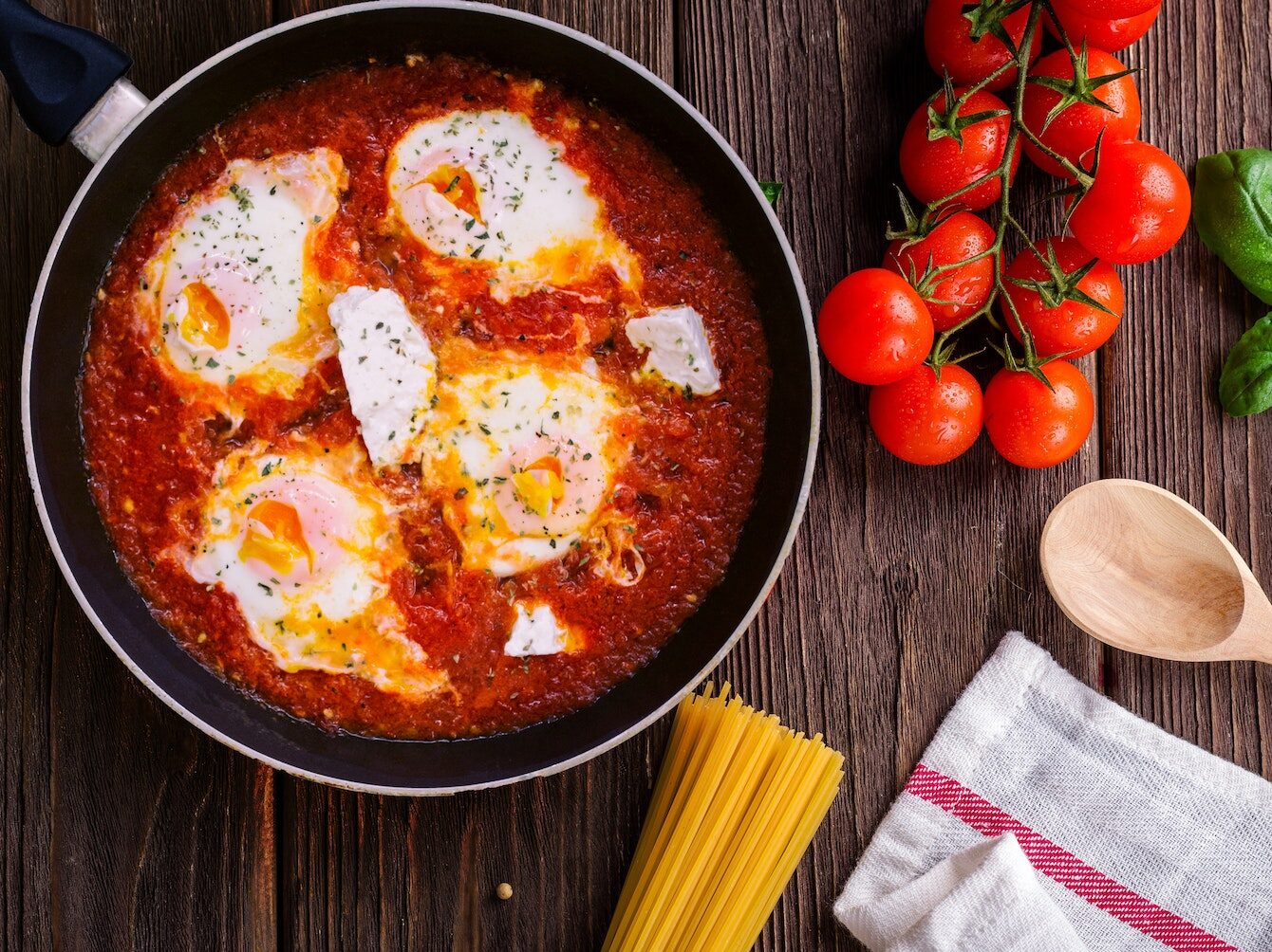 Black Frying Pan With Spaghetti Sauce Near Brown Wooden Ladle and Ripe Tomatoes