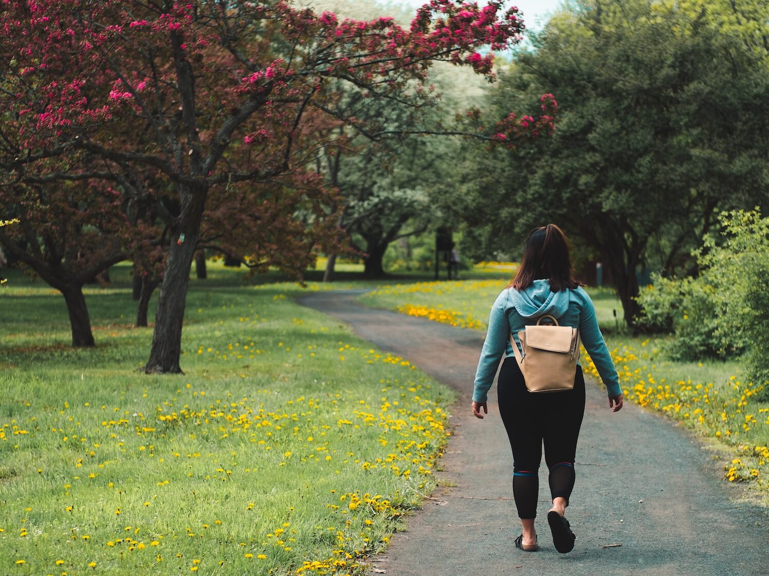 woman wearing blue jacket and black pants walking on grass field pathway