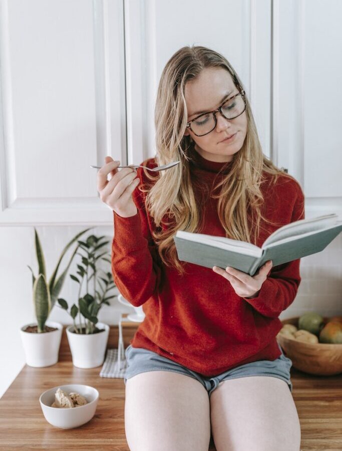 A Woman in Red Sweater Sitting on a Wooden Table while Reading a Book