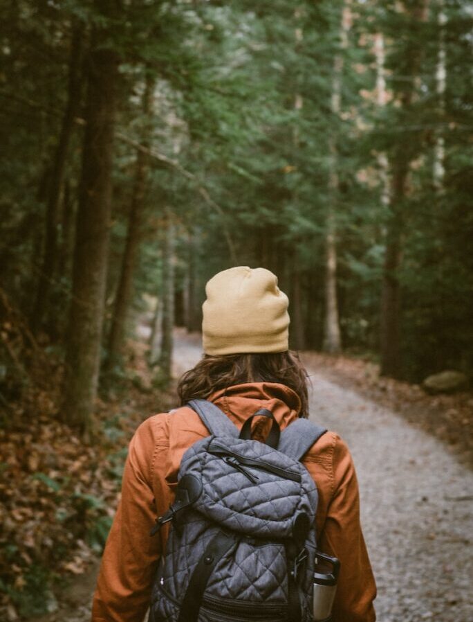 woman carrying backpack walking towards the forest