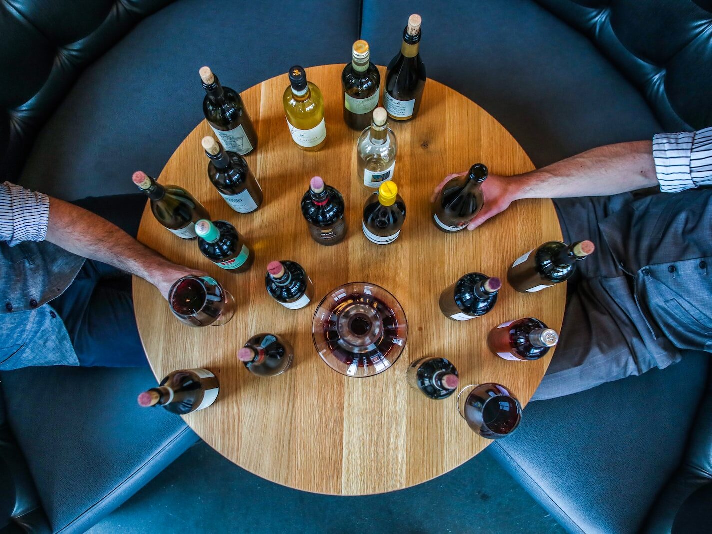 person holding glass bottle on round brown wooden table