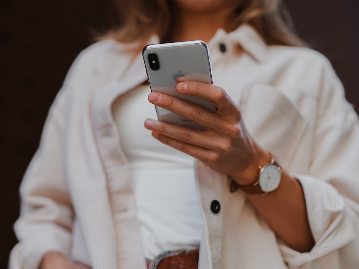 woman in white coat holding silver iphone 6