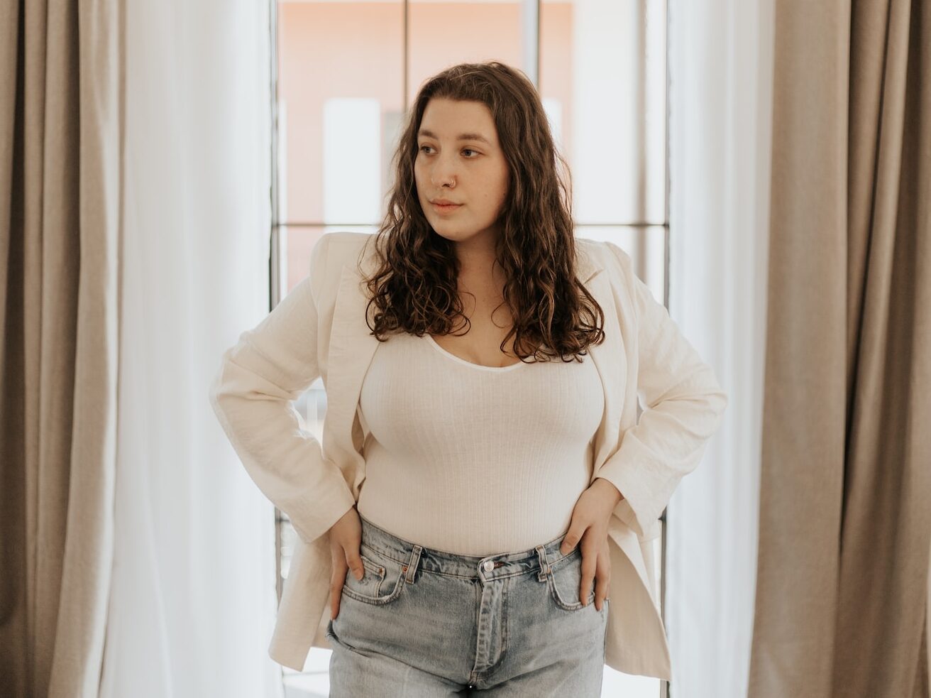 woman in white long sleeve shirt and blue denim jeans standing near window