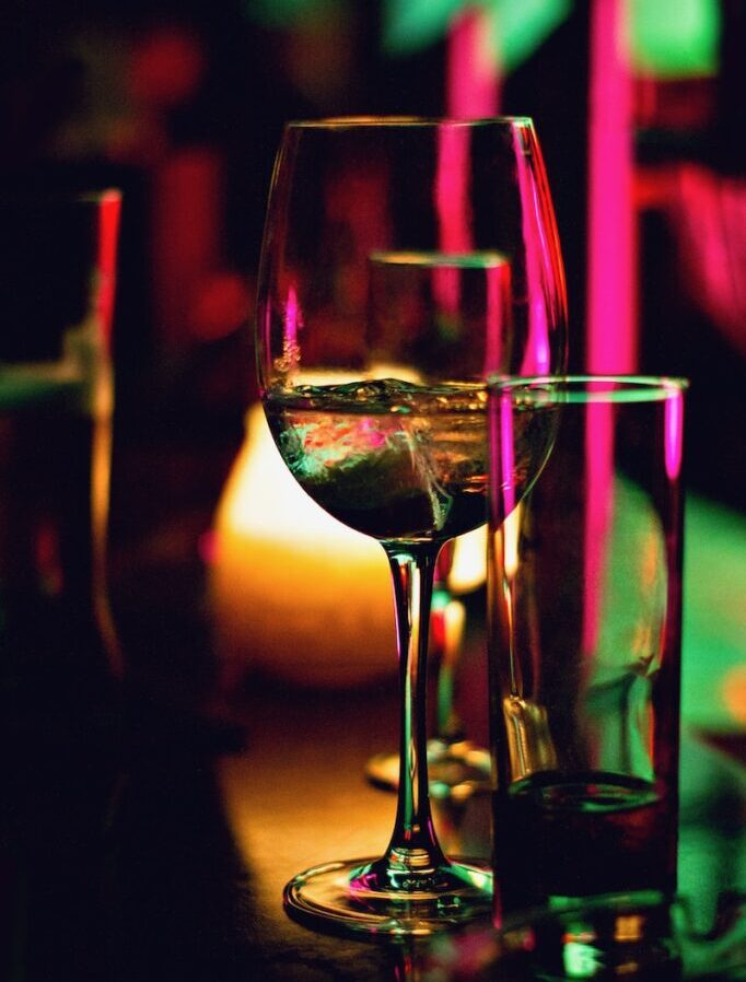 half filled wine glass beside half empty clear pint glass