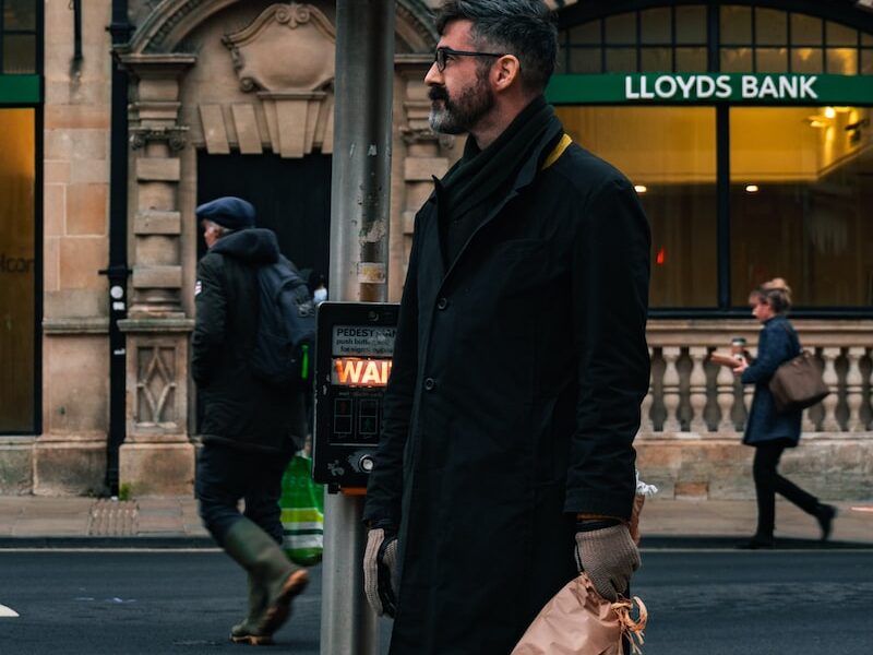 man in black coat holding green and red flower bouquet standing on sidewalk during daytime