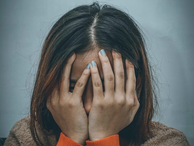 woman in brown sweater covering her face with her hand