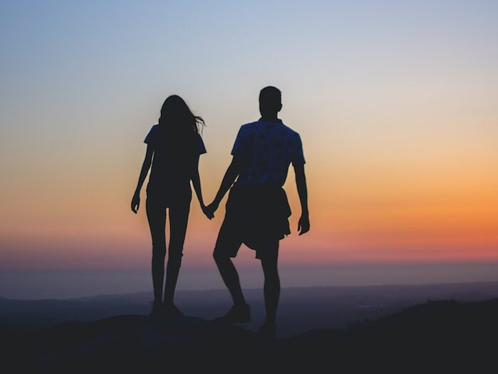 man and woman holding hands in silhouette photography