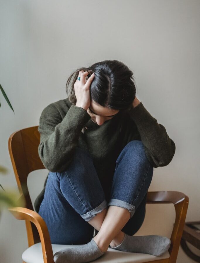 Anxious young woman cover wing ears with hands sitting on chair