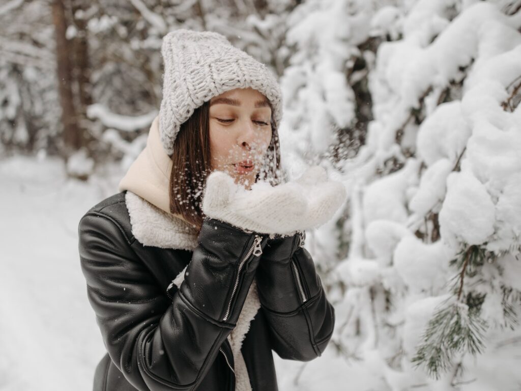 Photo of a Woman in a Black Leather Jacket Blowing Snow on Her Hands
