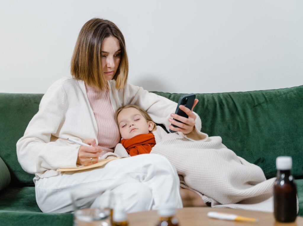 Woman Using Phone with Sick Child Sleeping in her Arms