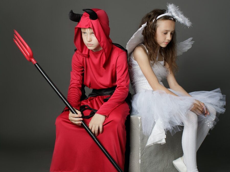 A Young Boy and Girl Wearing a Devil and Angel Costumes while Sitting on the Chair Back to Back