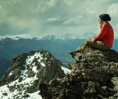 person sitting on rock across snow covered mountain under cloudy sky