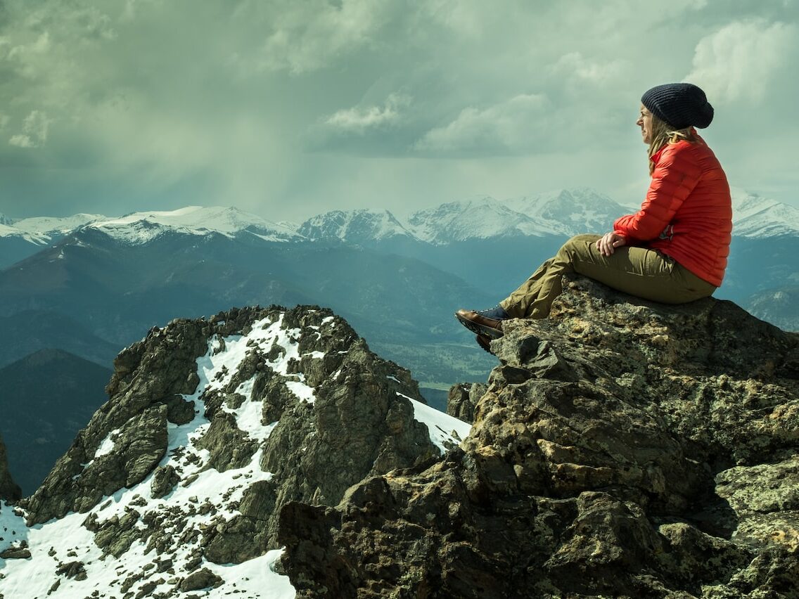 person sitting on rock across snow covered mountain under cloudy sky