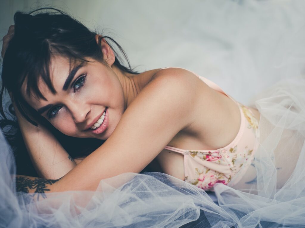 Close up Photo of Smiling Woman Wearing Pink Floral brassiere Lying on White Sheer Cloth