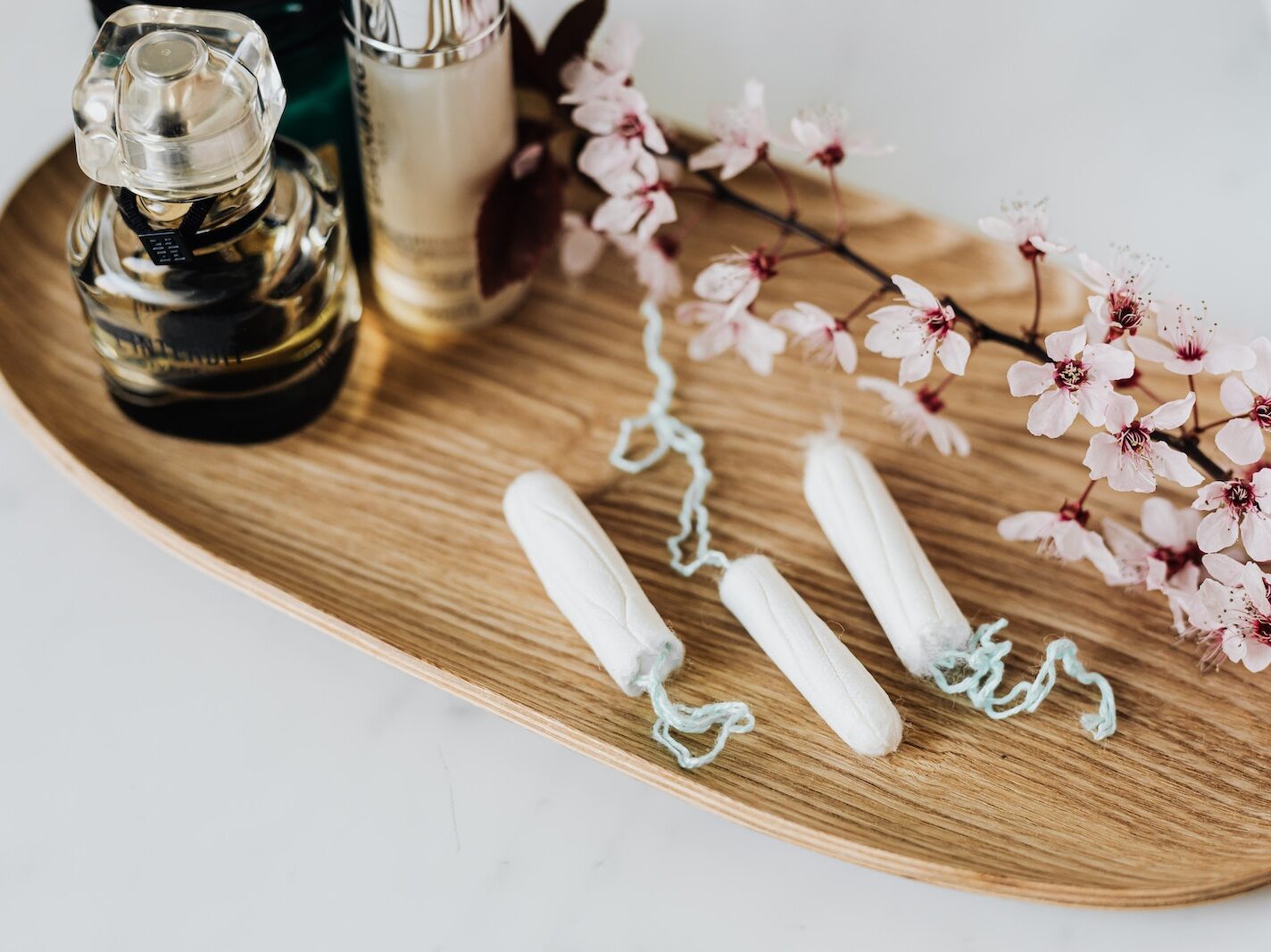 Wooden tray with perfume cosmetic products hygienic tampons and flower branch